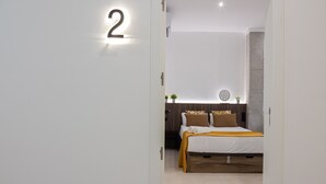 A modern hotel room with a bed, a wall-mounted number sign, and a small potted plant.