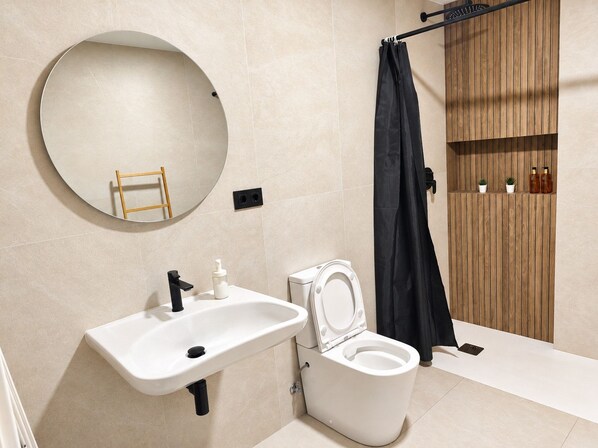A modern bathroom with a round mirror, a white sink, a toilet, and a wooden panel wall.