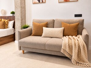 A neutral-toned sofa with a throw blanket, a small potted plant, and a wall-mounted light switch.