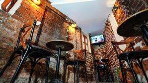A brick-walled bar area with multiple black metal chairs and tables, a television mounted on the wall, and decorative flowers. - Squit Suits Hotel (İstanbul)