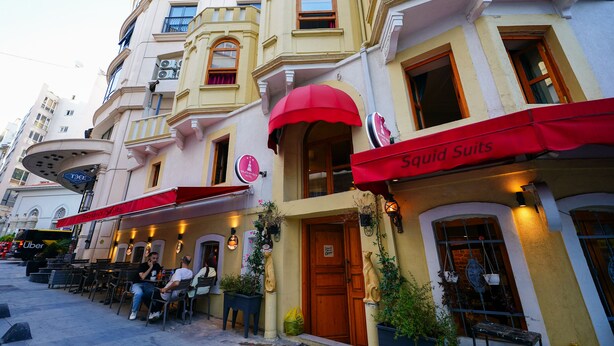 A building with a red awning labeled "Squid Sails" and a sign for "TAXI". - Squit Suits Hotel (İstanbul)