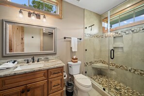 A bathroom with a large mirror, wooden vanity, marble countertop, toilet, and a glass-enclosed shower area. - River Rock - 1mile to downtown Banner Elk, pets (Banner Elk)