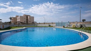 A swimming pool with a clear blue water, surrounded by a concrete deck, and a building in the background.