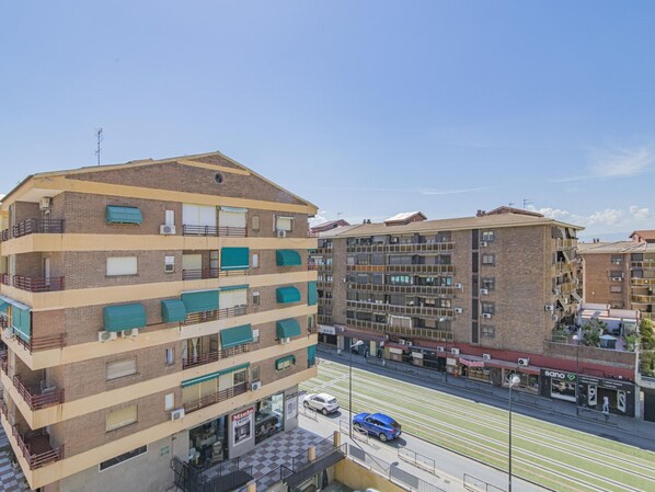 A multi-story residential building with balconies, a street view, and a clear sky. - 2-Bedroom Retreat with Terrace in Granada - Steps from Metro and Bus (Granada)