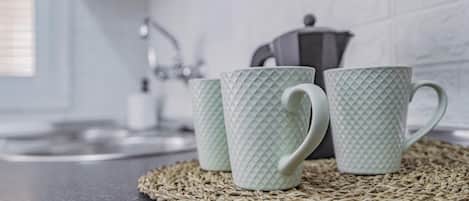 Three textured mugs on a woven placemat in a kitchen with a white tiled backsplash and a kettle in the background.
