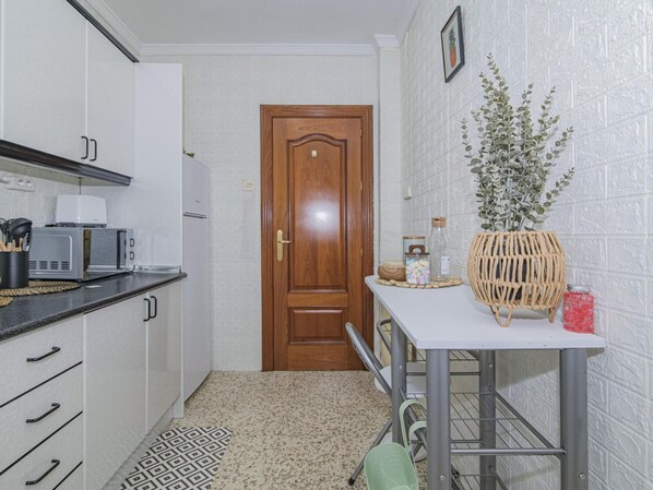Cozinha compacta com armários brancos, micro-ondas, torradeira e porta de madeira.
