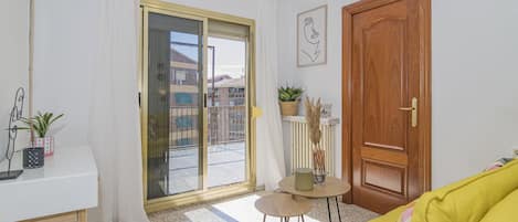 Un salón luminoso con un sofá amarillo, una mesa blanca y un ventanal corredera que da a un balcón.