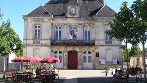A historic building with a clock tower, a red door, and a balcony with flowers. - 5-minute walk from Aigre, 60m2 ground floor apartment (Aigre)