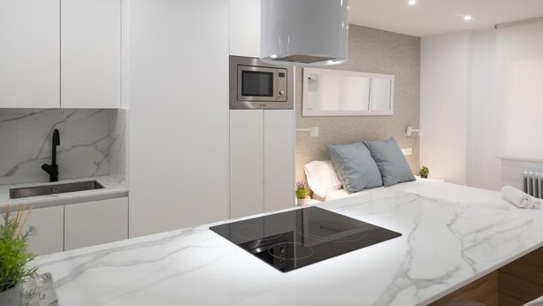 Une cuisine moderne avec des meubles blancs, un four à micro-ondes encastré et un grand îlot central doté d’une plaque de cuisson à induction noire.