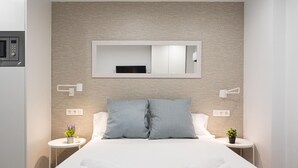Une chambre d’hôtel moderne avec un grand lit, deux oreillers, une table de chevet agrémentée d’une plante et un miroir fixé au mur.