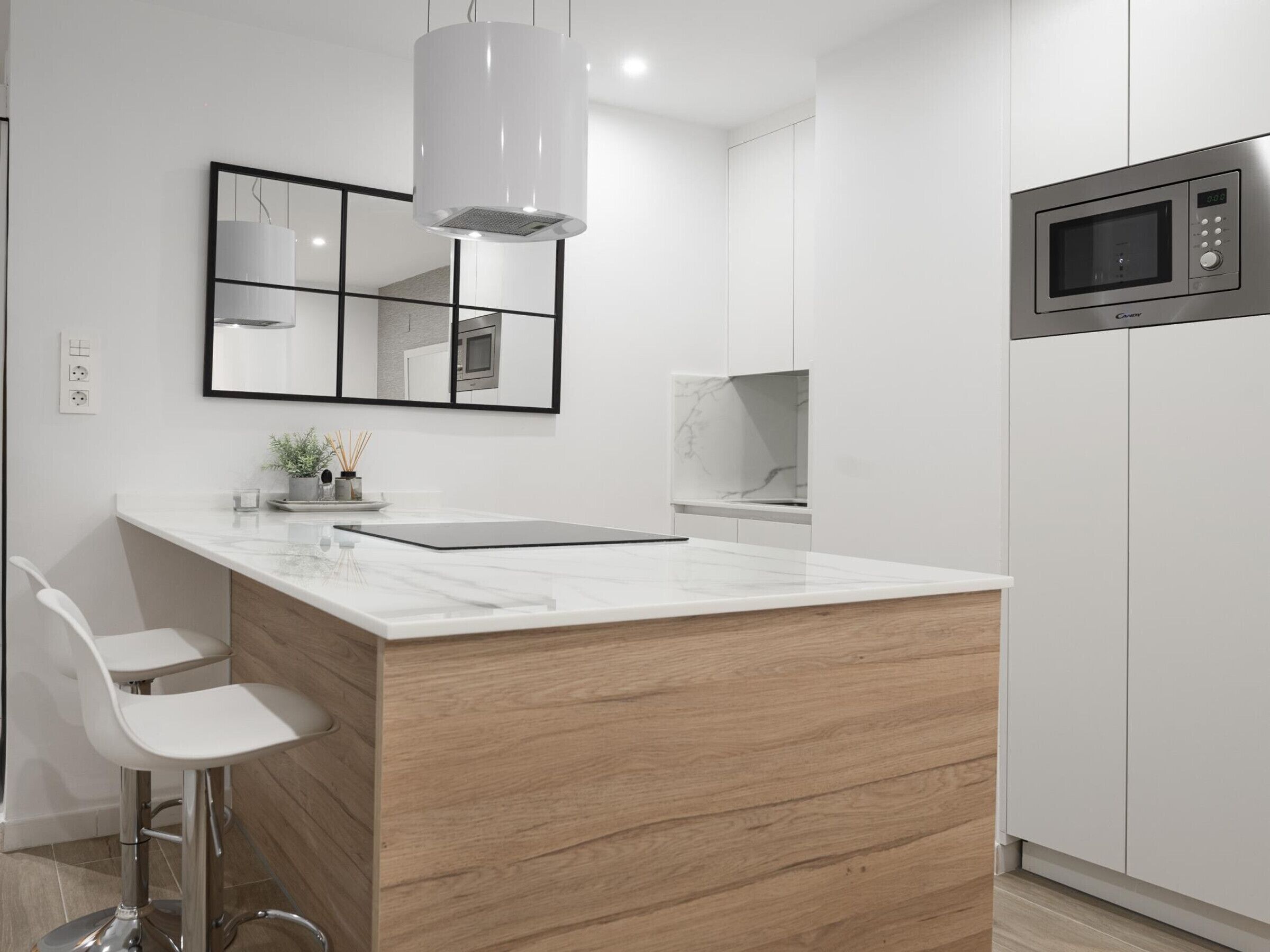 Une cuisine moderne dotée d’un plan de travail en marbre, de meubles en bois, d’un four à micro-ondes encastré et d’un luminaire suspendu.