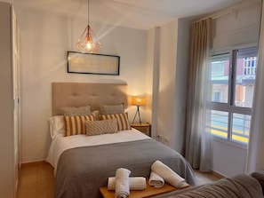 Ein ordentlich eingerichtetes Hotelzimmer mit einem großen Bett, einer Nachttischlampe und Blick auf die Straße durch ein Fenster.