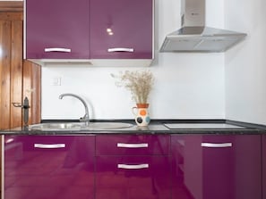 A kitchen with purple cabinets, a stainless steel sink, and a modern range hood.