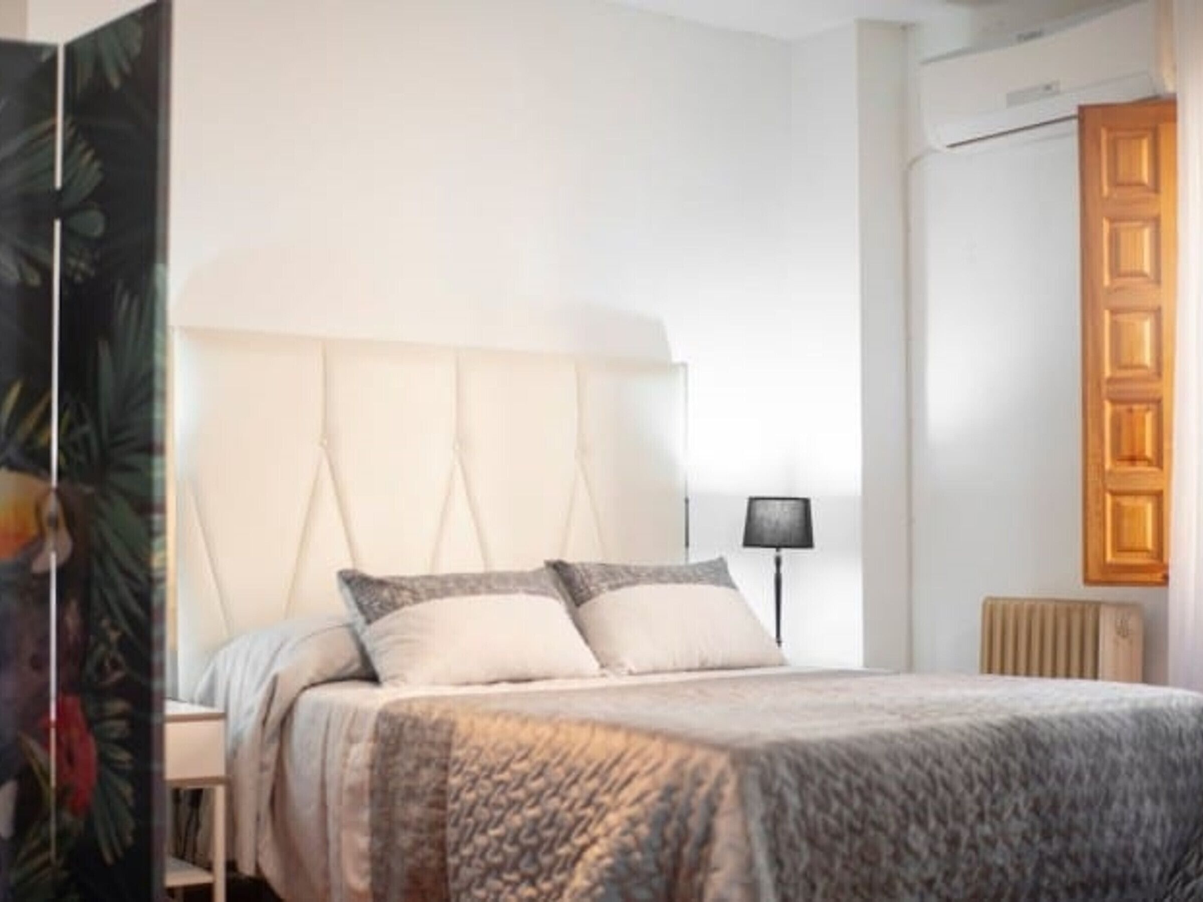 Ein Schlafzimmer mit einem großen Bett, einem Kopfteil, einem Nachttisch, einer Lampe und einem Heizkörper.