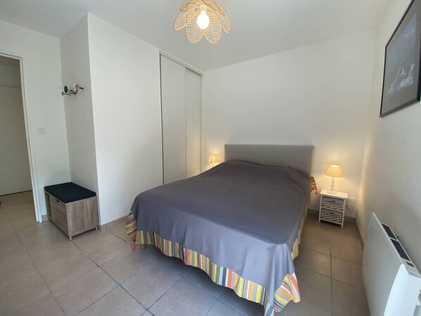 A bedroom with a bed, a nightstand, a lamp, a small stool, and a door.