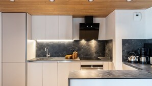 A modern kitchen with white cabinetry, a black countertop, and a wooden ceiling. - Luxury apartment spa & parking, Les Saisies, 11 people (Les Saisies)