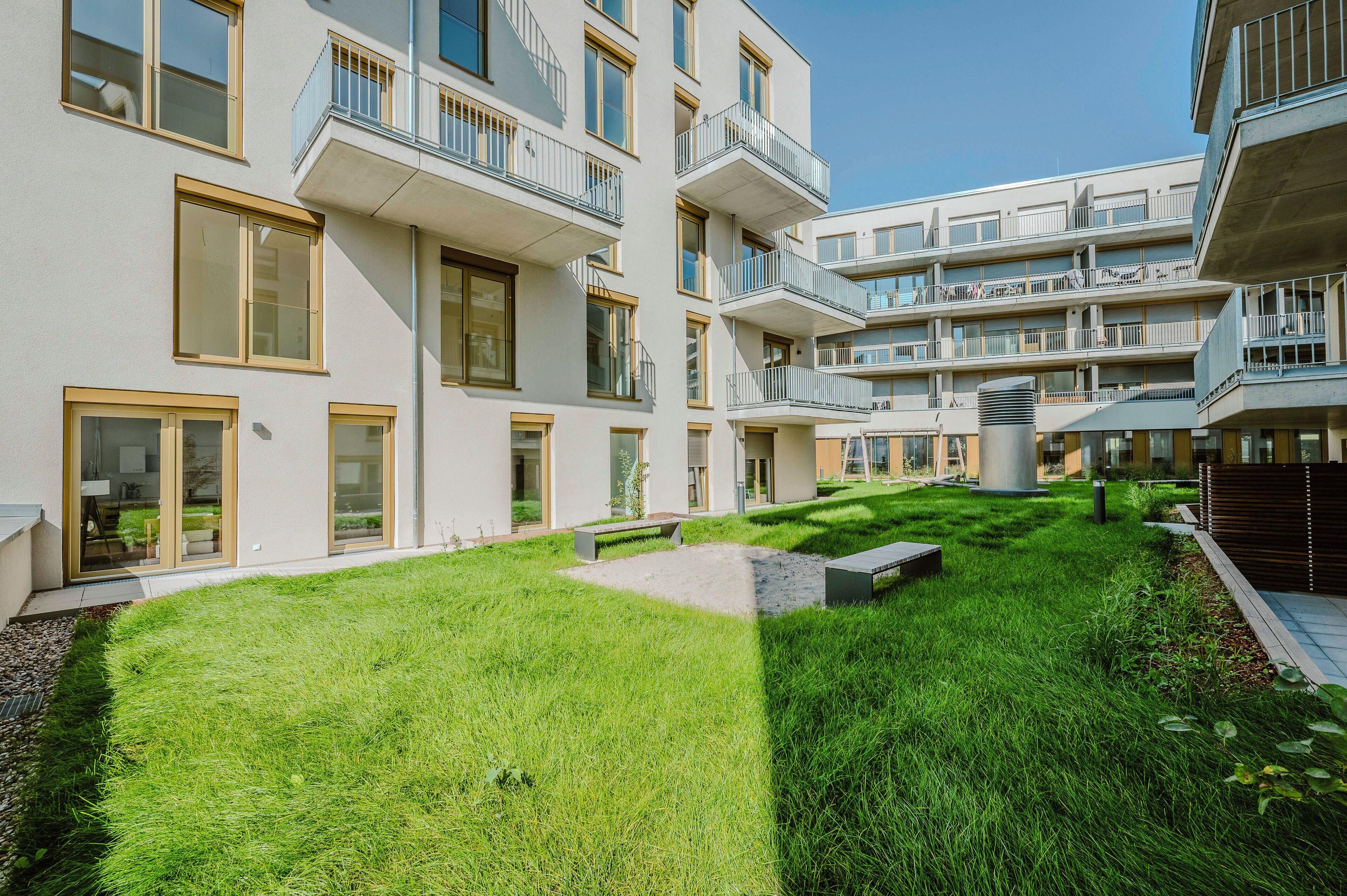 Ein modernes Mehrfamilienhaus mit mehreren Balkonen, einem gepflegten Rasen und blauem Himmel.