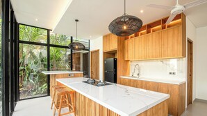 Une cuisine moderne dotée d’un grand îlot central, de meubles en bois et offrant une vue sur la verdure environnante.