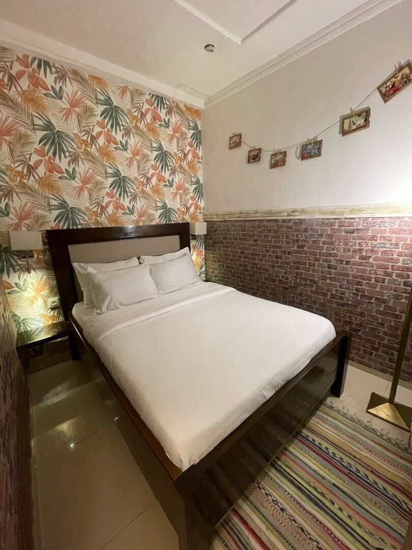 Una cama con ropa blanca, una pared con diseño de ladrillo y una alfombra a rayas.