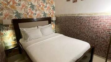 Una cama con ropa blanca, una pared con diseño de ladrillo y una alfombra a rayas.