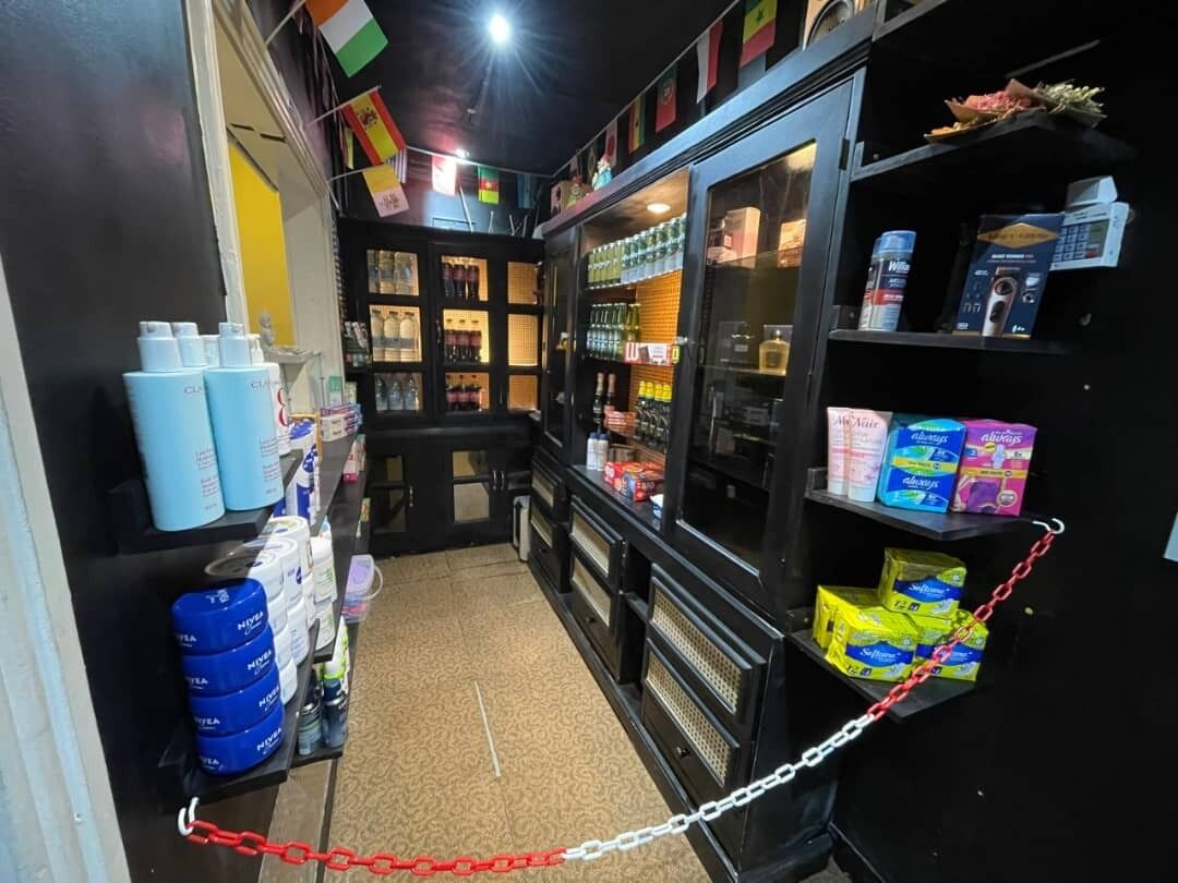 Un pasillo estrecho con estantes llenos de diversos productos, una barrera de cadena y una vitrina con artículos.