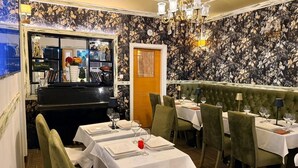Un interior de restaurante con mesas dispuestas para comer, un piano y un diseño de papel tapiz floral.