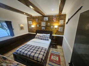 A bedroom with a bed, bedside tables, a window with curtains, wooden wall paneling, and wall-mounted lamps. - The Retreat (Yaoundé)