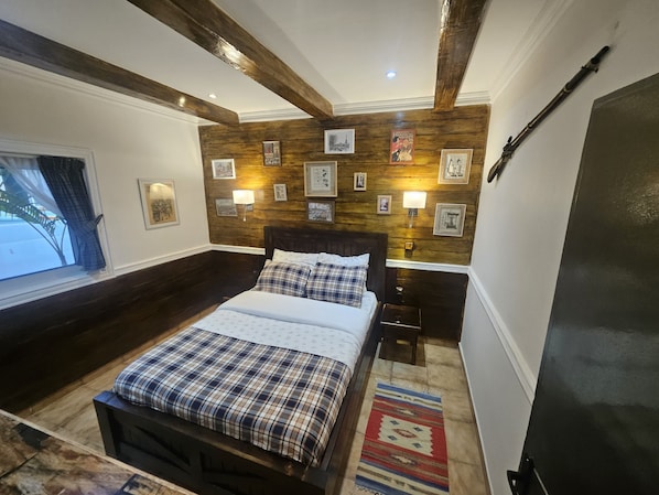 A bedroom with a bed, bedside tables, a window with curtains, wooden wall paneling, and wall-mounted lamps.