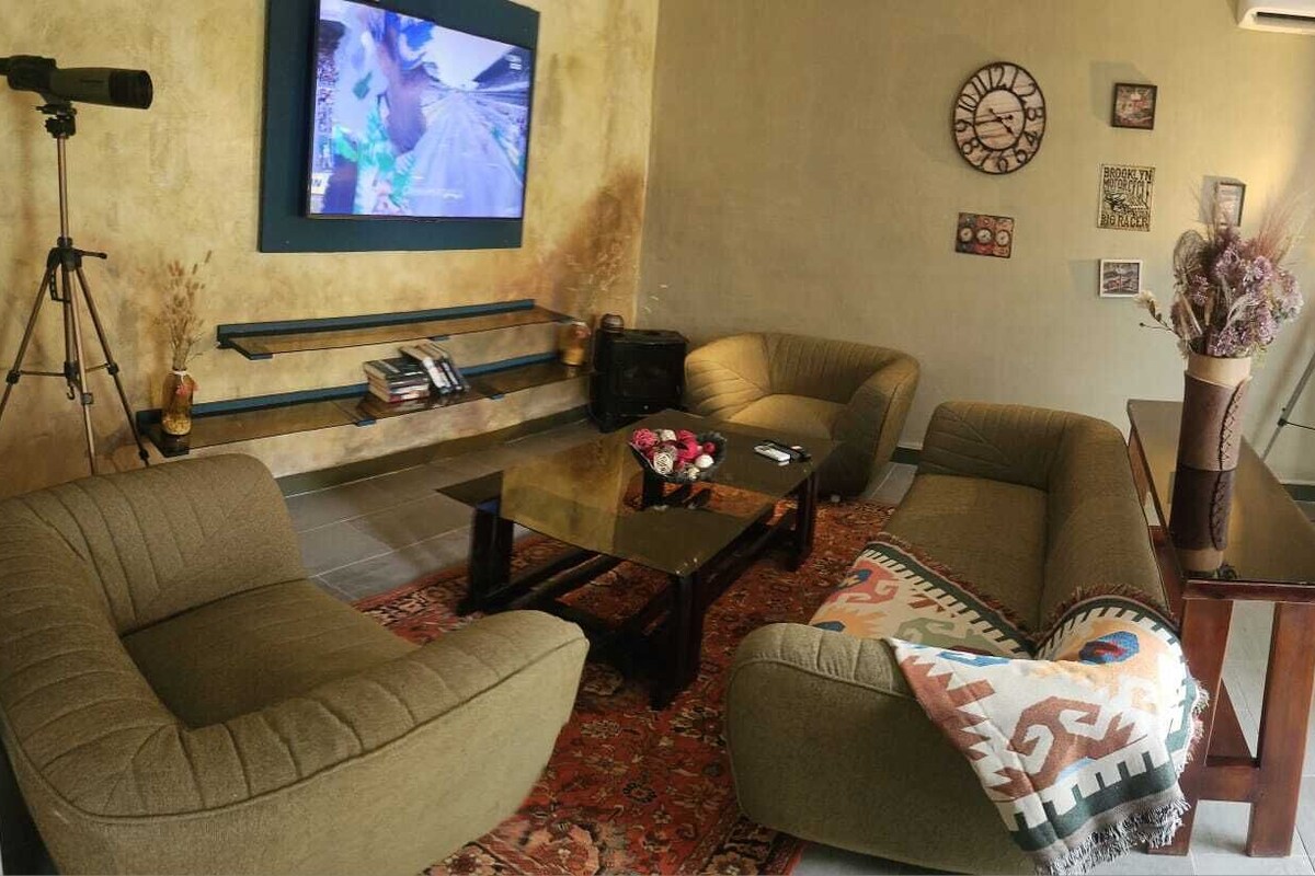 A living room with a sofa, armchair, coffee table, and a television mounted on the wall.
