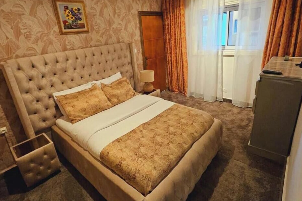 A bedroom with a large bed, a bedside table, a lamp, and a dresser.