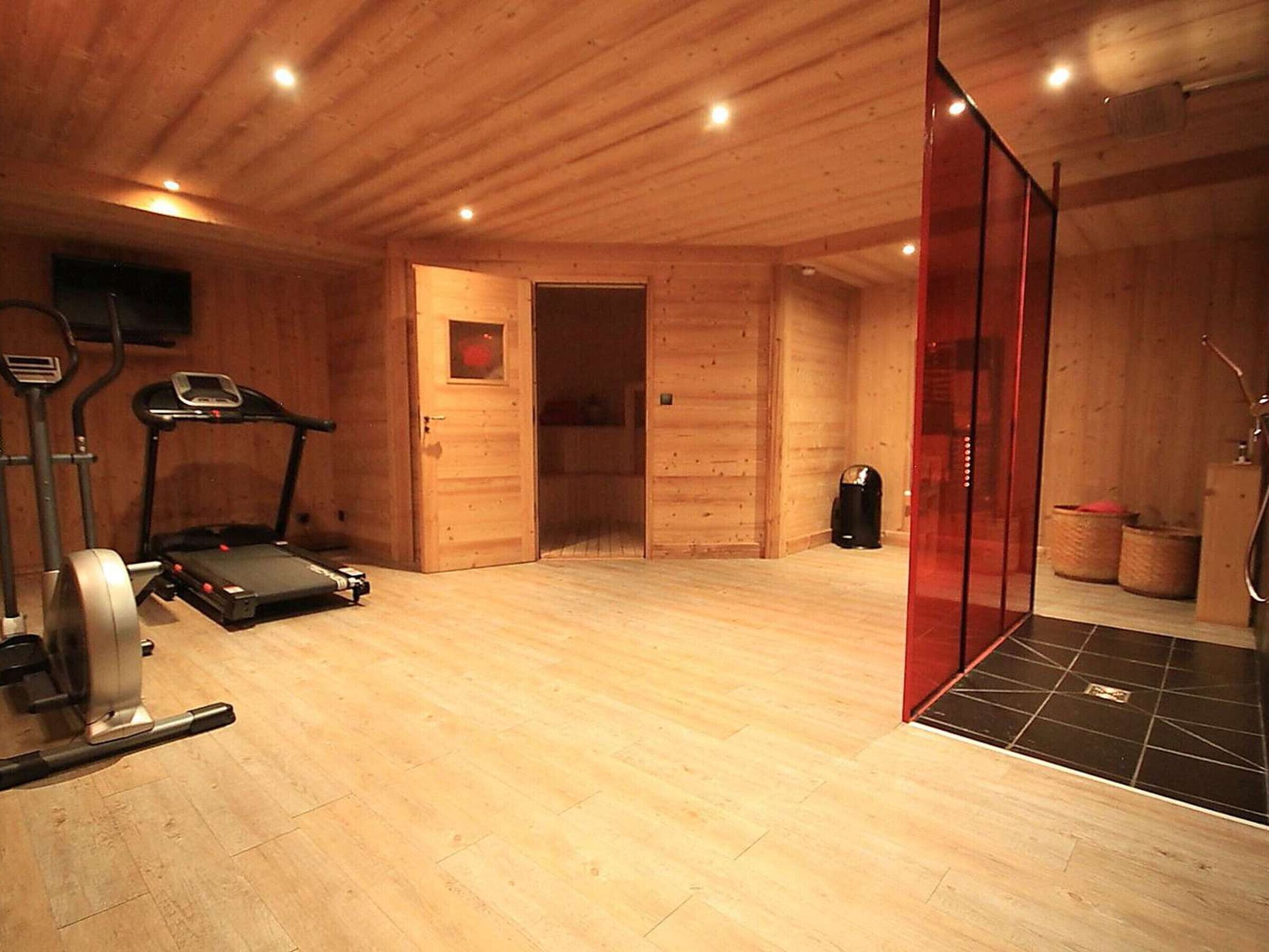 Ein Fitnessraum mit Trainingsgeräten, einer Duschkabine und Holzwänden.