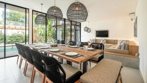 Een moderne eetruimte met een lange houten tafel, zwarte stoelen en gevlochten hanglampen.