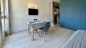 A dining area with a table set for two, a television mounted on the wall, and a closet with shelves.