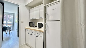 A compact kitchen with white cabinets, a microwave, a toaster, and a refrigerator.