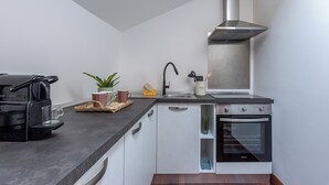 A compact kitchen with a modern stove, a built-in oven, a stainless steel range hood, and a minimalist countertop. - Kadì Apartment by Wonderful Italy (Palermo)