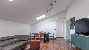 A modern living room with a grey sofa, a round dining table with chairs, a small ottoman, and a flat-screen TV on a green cabinet. - Kadì Apartment by Wonderful Italy (Palermo)