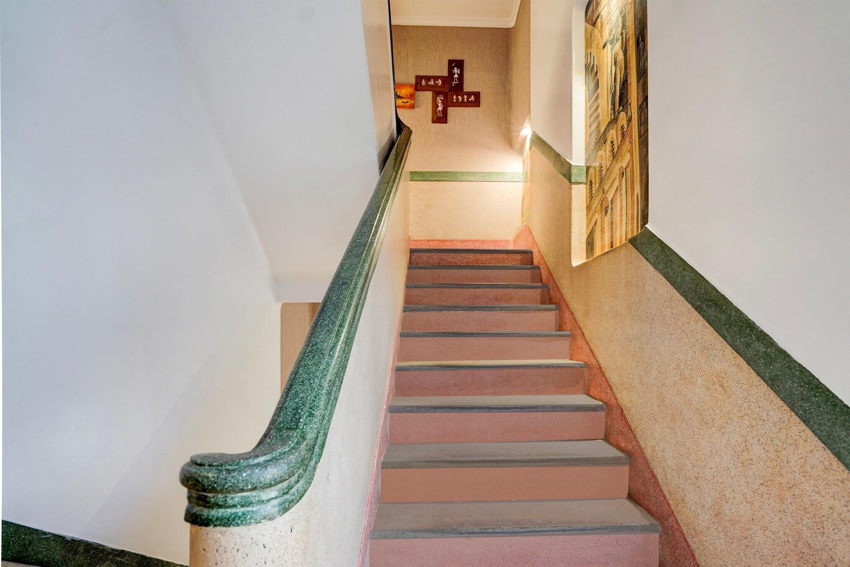 Una escalera con barandilla de mármol verde, paredes color beige y un mural a la derecha.