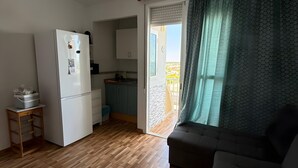 Un espace de vie compact comprenant un coin cuisine, un canapé et une porte-fenêtre coulissante donnant sur un balcon.