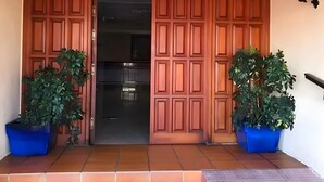 Une porte en bois dotée d’un système coulissant, deux plantes en pot et un luminaire fixé au mur.