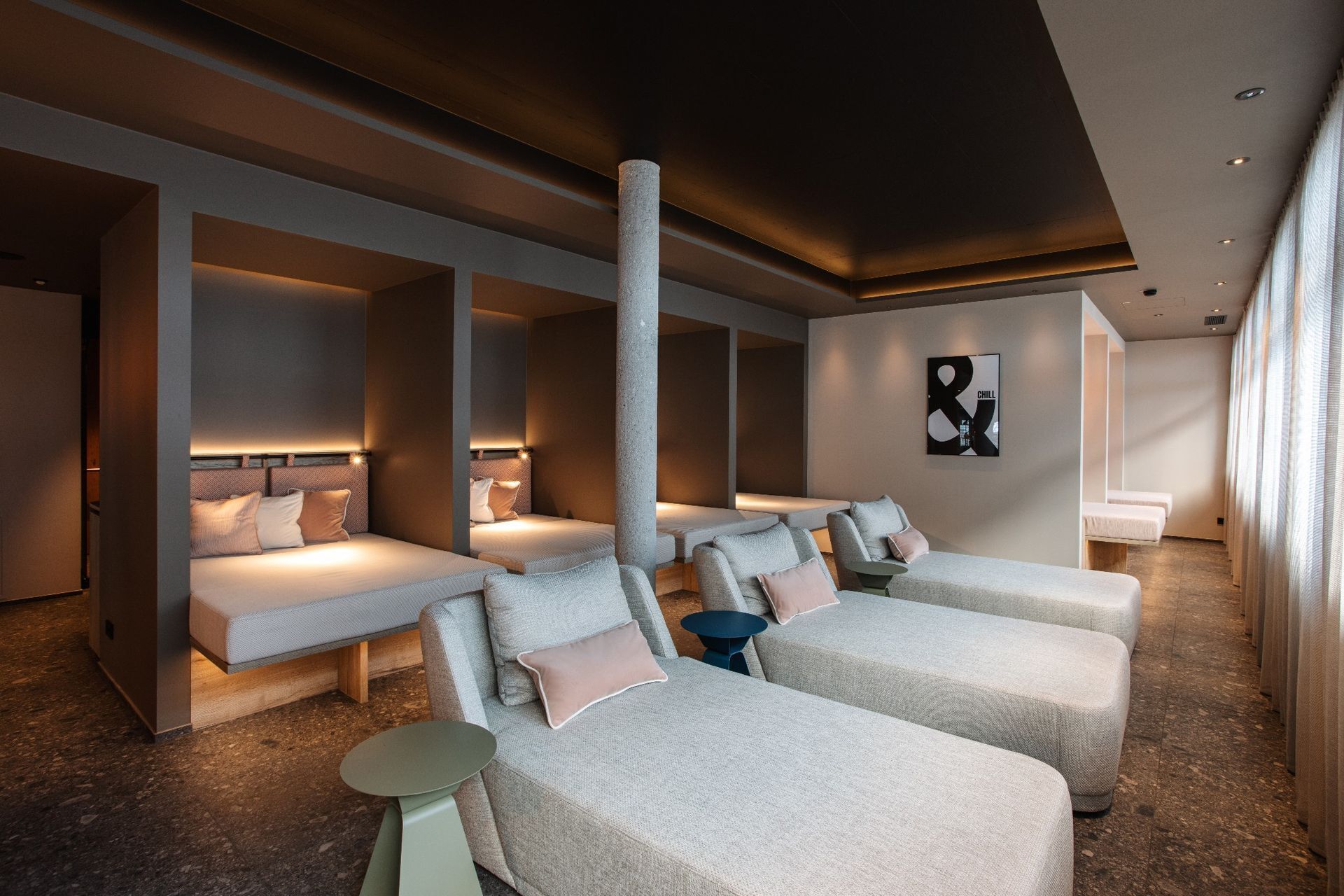 A modern spa room with two large, cushioned seating areas, a central pillar, and a wall-mounted artwork.