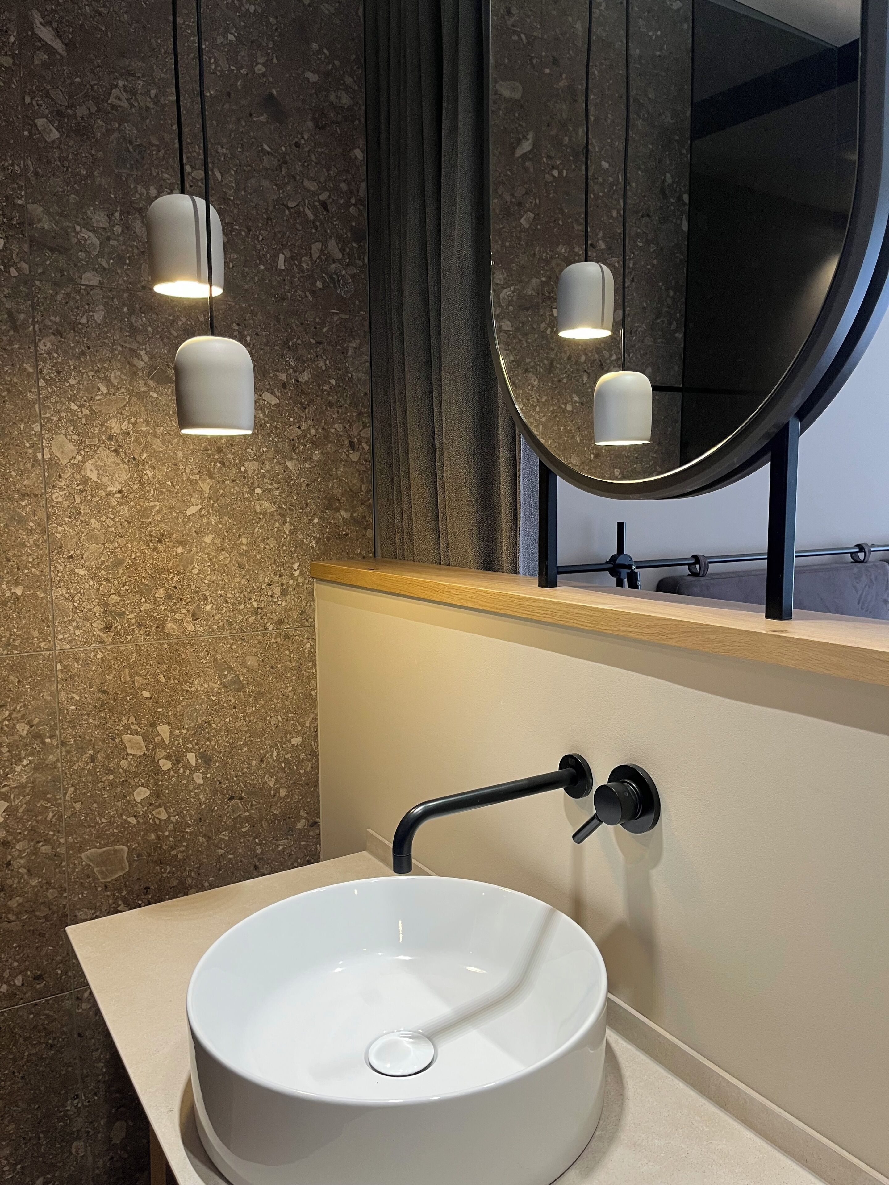 Une salle de bain avec un lavabo blanc, un miroir et des luminaires suspendus.