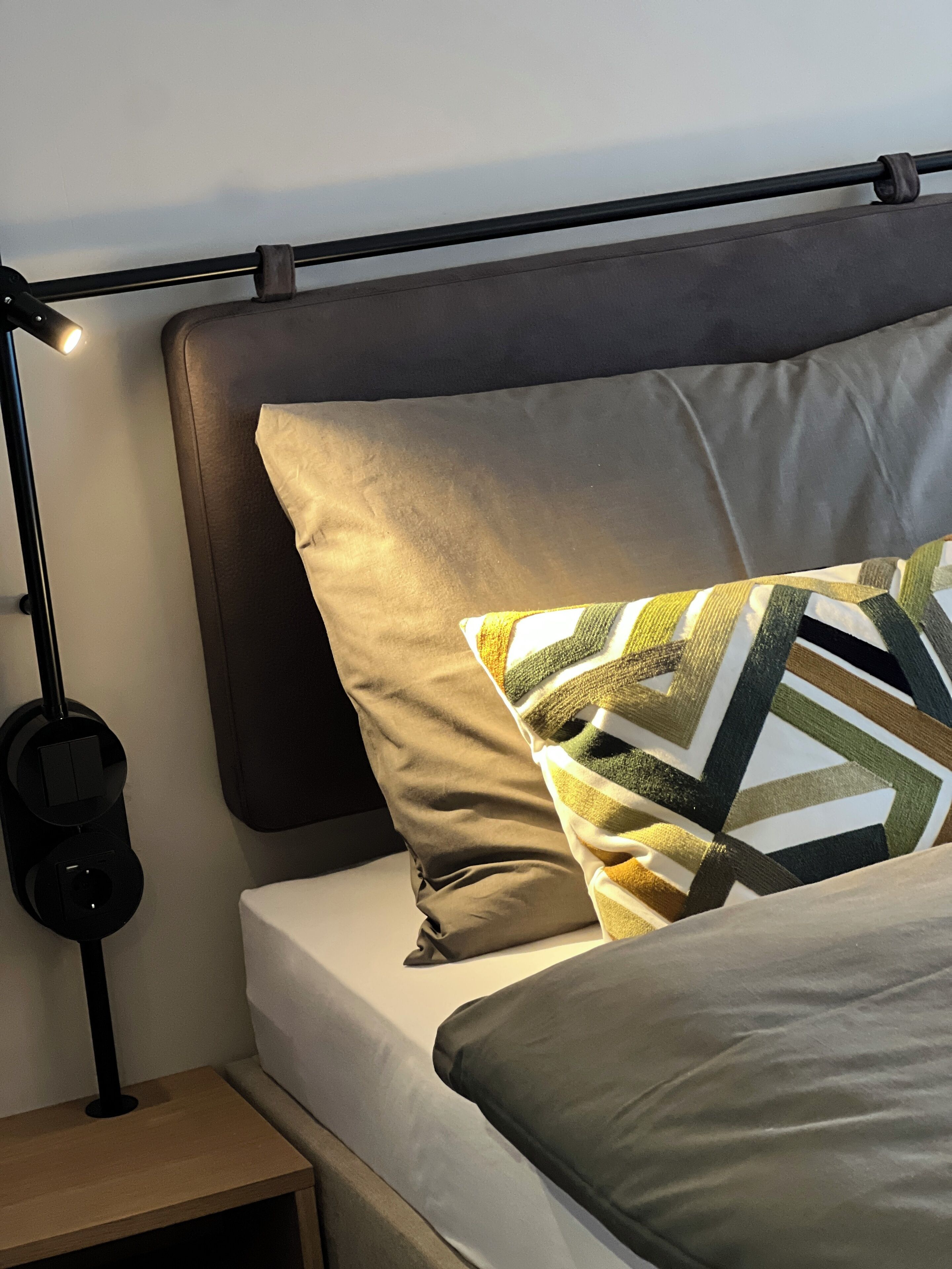 Una cama bien hecha con una almohada, una lámpara de noche y una mesita de noche de madera.