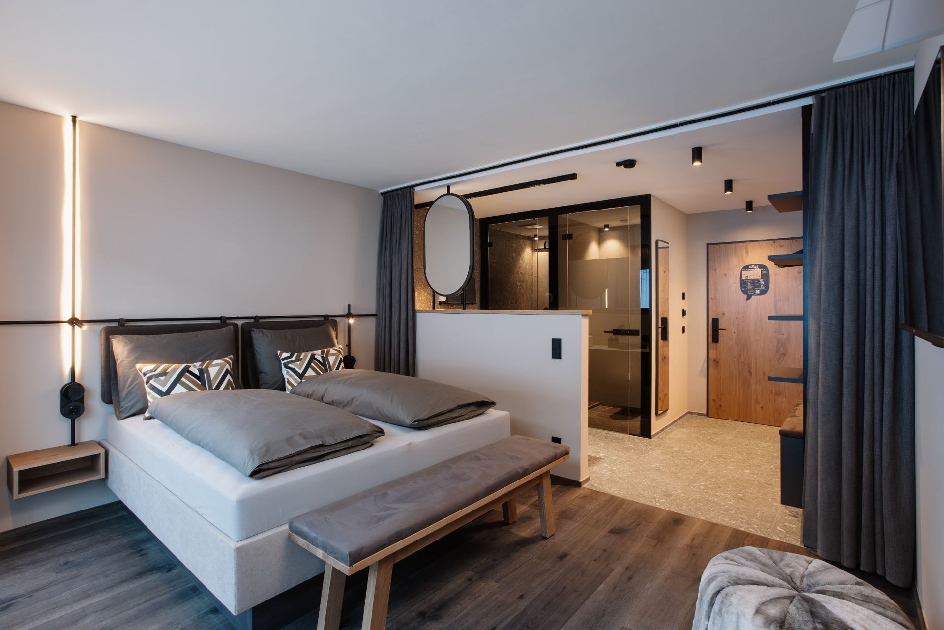 A modern bedroom with a bed, bedside tables, a bench, and a mirror.