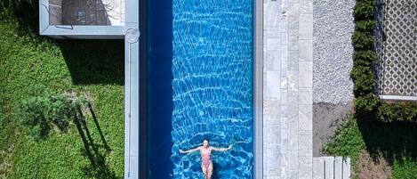 A rectangular swimming pool with a person swimming, surrounded by a stone deck and grass.