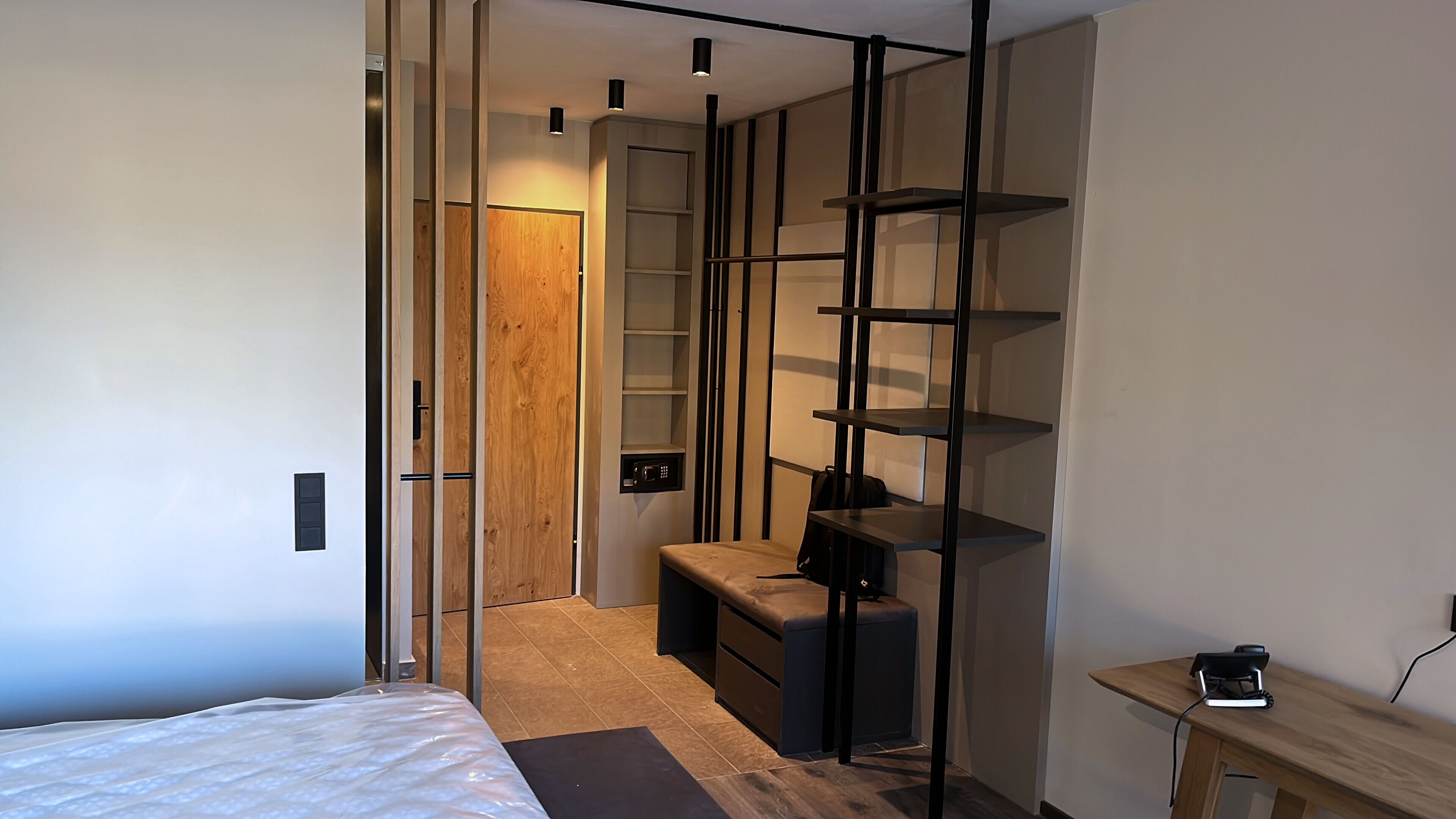 Quarto moderno com cama, um banco, escrivaninha e guarda-roupa com prateleiras.