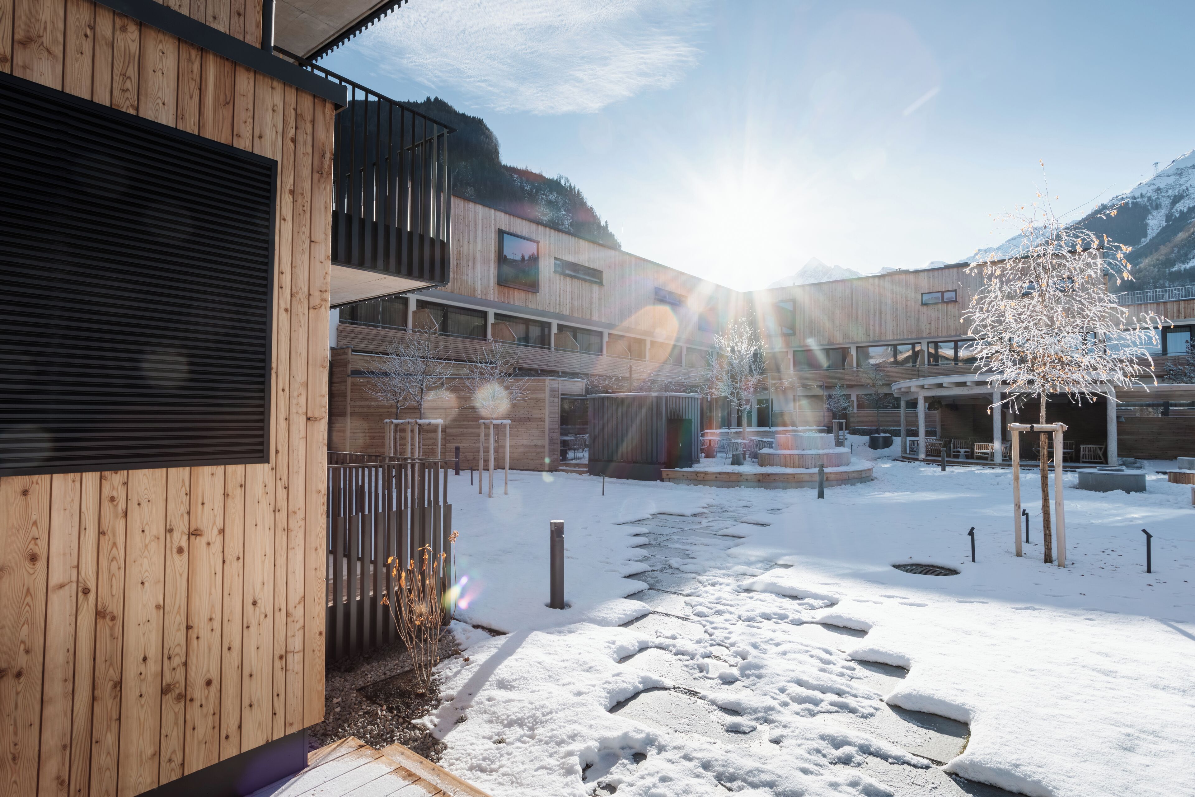 Un patio cubierto de nieve con edificios de madera, cielo despejado y montañas al fondo.