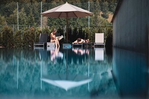 A swimming pool with lounge chairs and an umbrella. - Revier Boutique Hotel Kaprun (Kaprun)