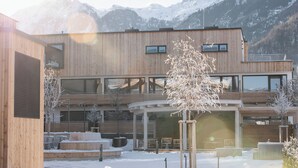 Un bâtiment moderne doté d’une façade en bois, de grandes fenêtres et d’un espace extérieur couvert aménagé avec des sièges.
