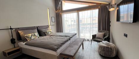 Un dormitorio moderno con una cama grande, un banco, una silla y un televisor montado en la pared.