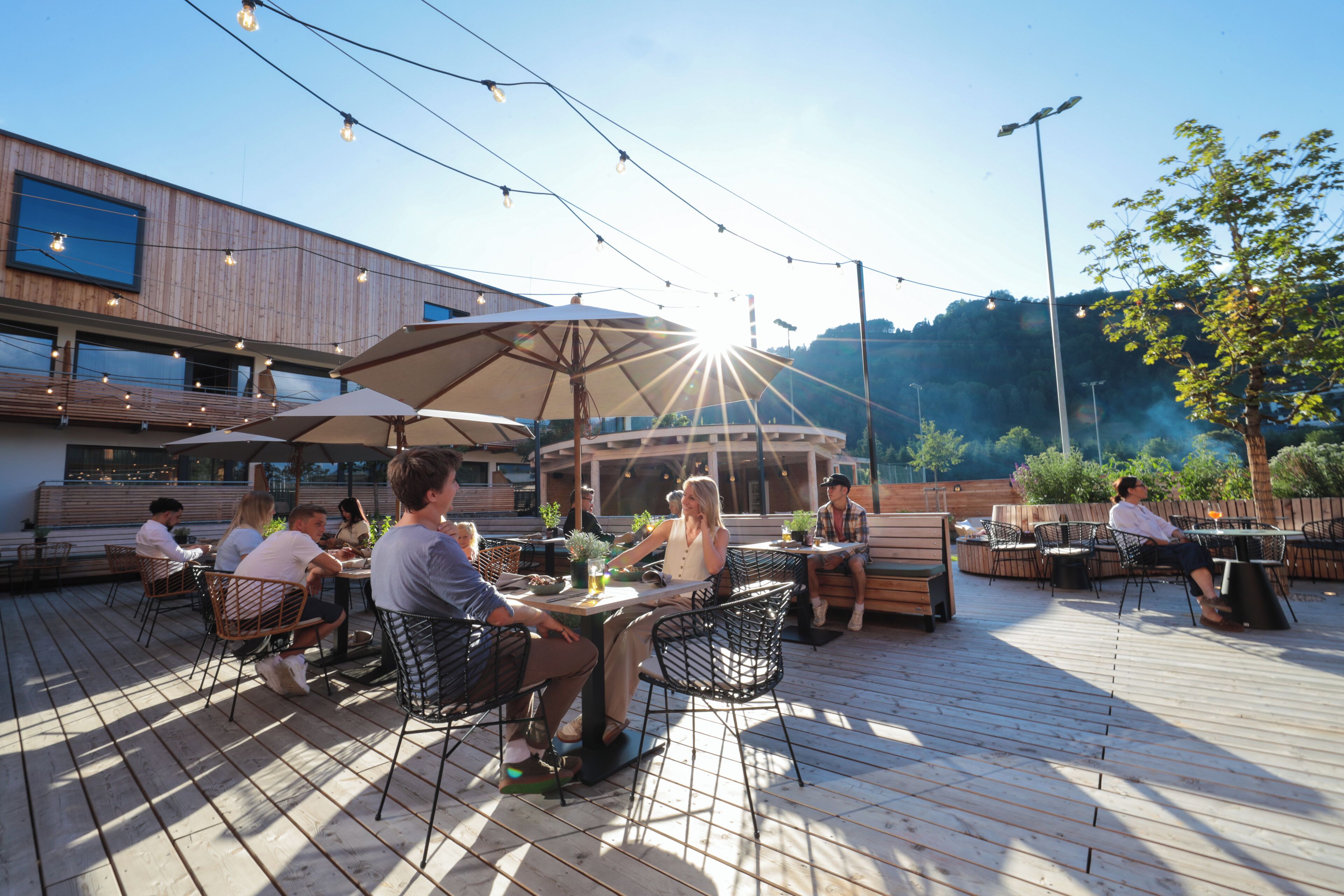 An outdoor seating area with tables and chairs, surrounded by string lights and umbrellas.